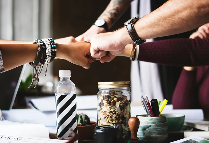 Employee engagement - multiple employees doing a teamwork salute over a desk