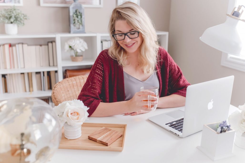 Blonde woman sitting in home office at desk while using Apple laptop