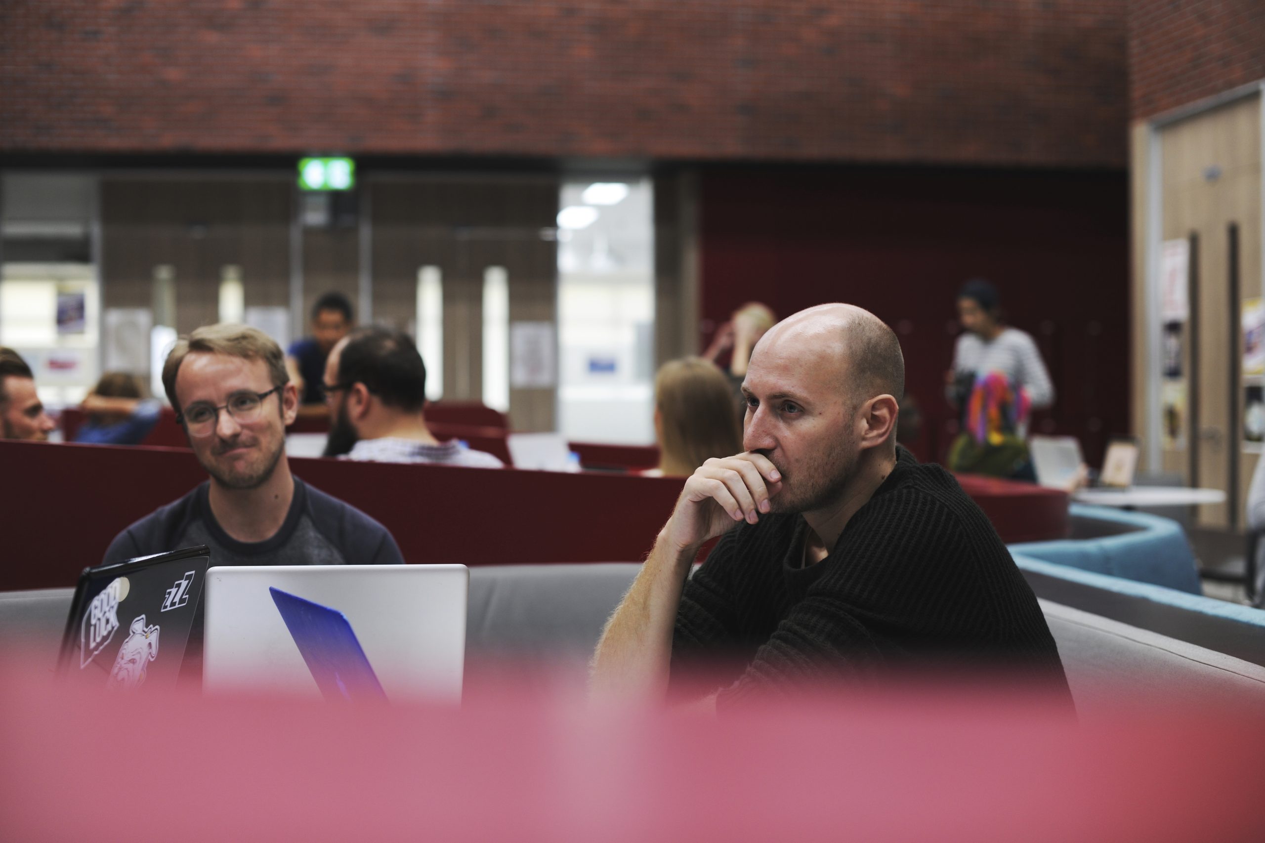 Employee engagement vs employee experience: Two employees thinking in a modern office with laptops and red brick walls.