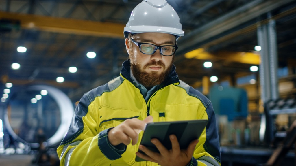 Remote worker - factory worker wearing hard hat and using a touchscreen tablet computer