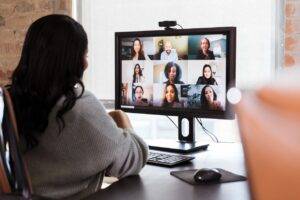 A group of diverse business colleagues participate in a virtual staff meeting during the COVID-19 pandemic. An African American businesswoman participates in the virtual event from her office.