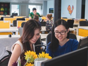 two women sitting in front of computer and smiling with flowers around