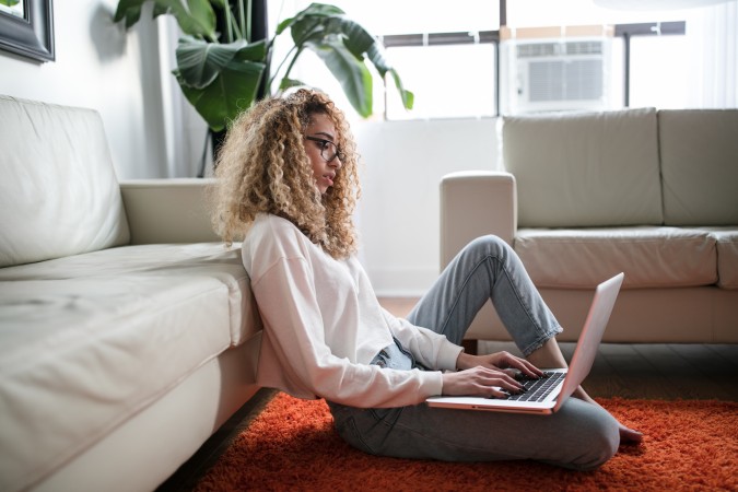 Intranet benefits - woman sitting and working with laptop computer in front of a grey couch