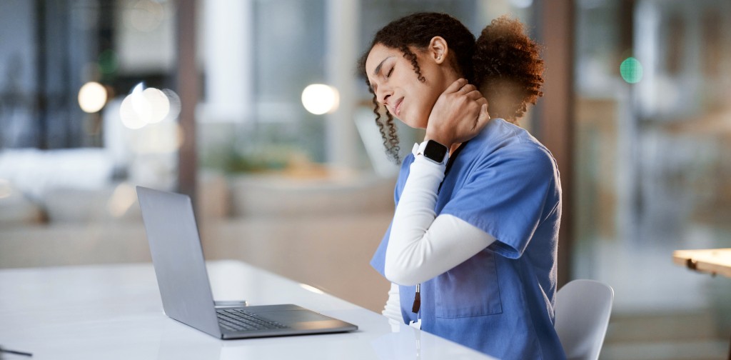 Healthcare frontline worker female doctor looking at laptop, massaging neck, and looking tired while sitting in hospital