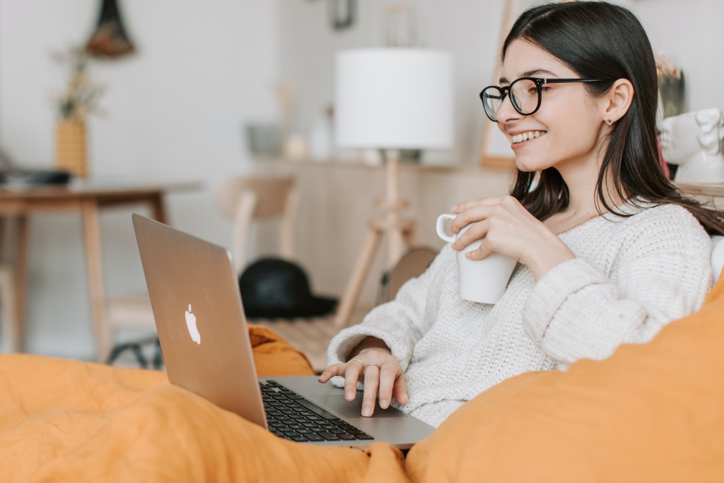 Financial services employee wfh woman sitting on couch with laptop and coffee