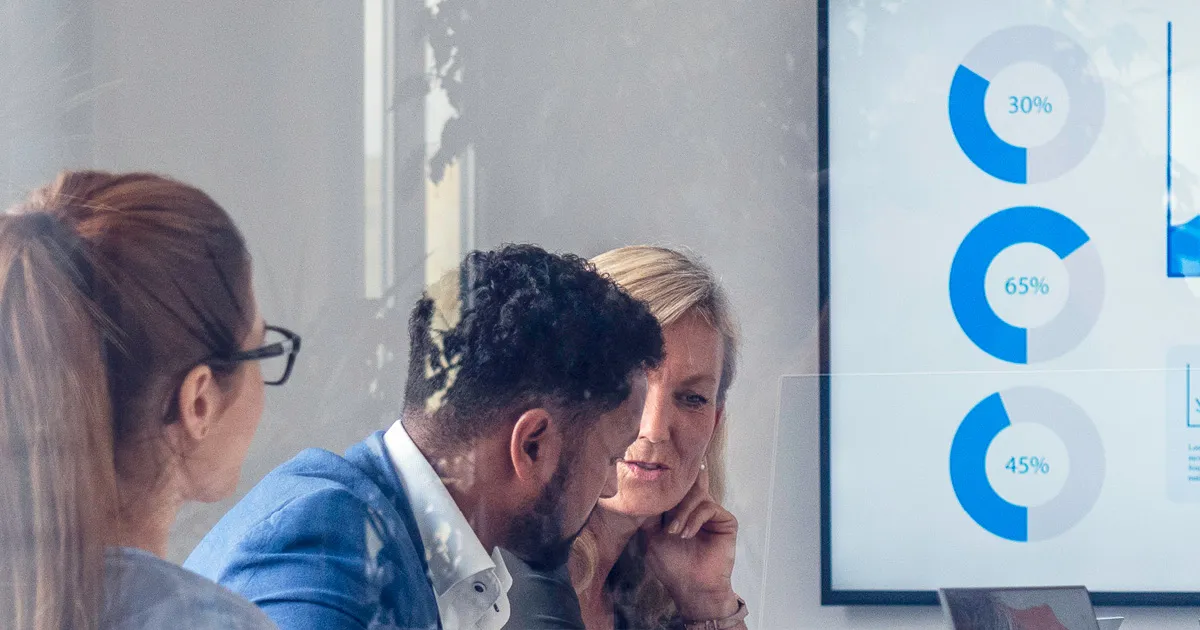 Intranet ROI - two women and one man having a discussion with screen showing pie charts in the background