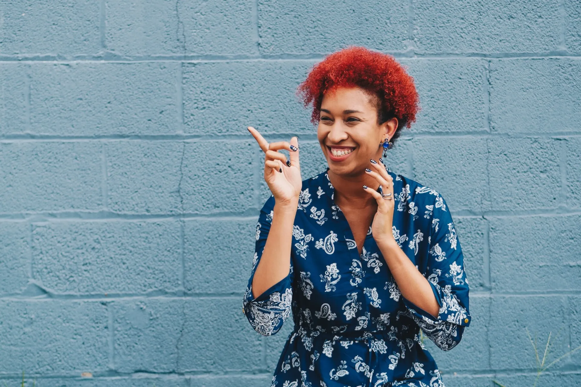 Woman standing in front of wall pointing and smiling