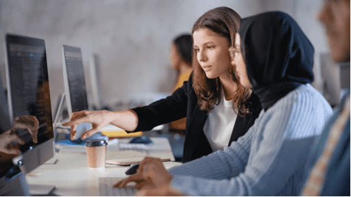 Preboarding - two female employees working together in front of a desktop computer in an open office space