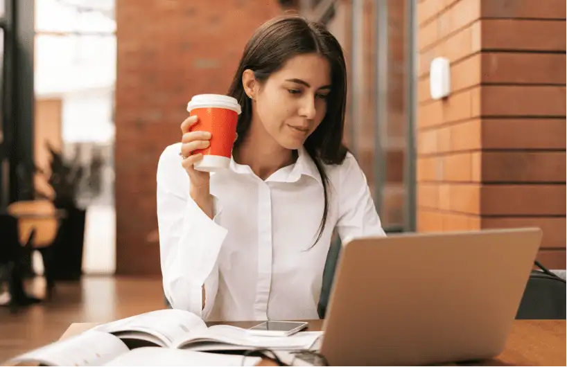 Skills gap - woman in white shirt holding coffee cup and working on laptop at outdoor table