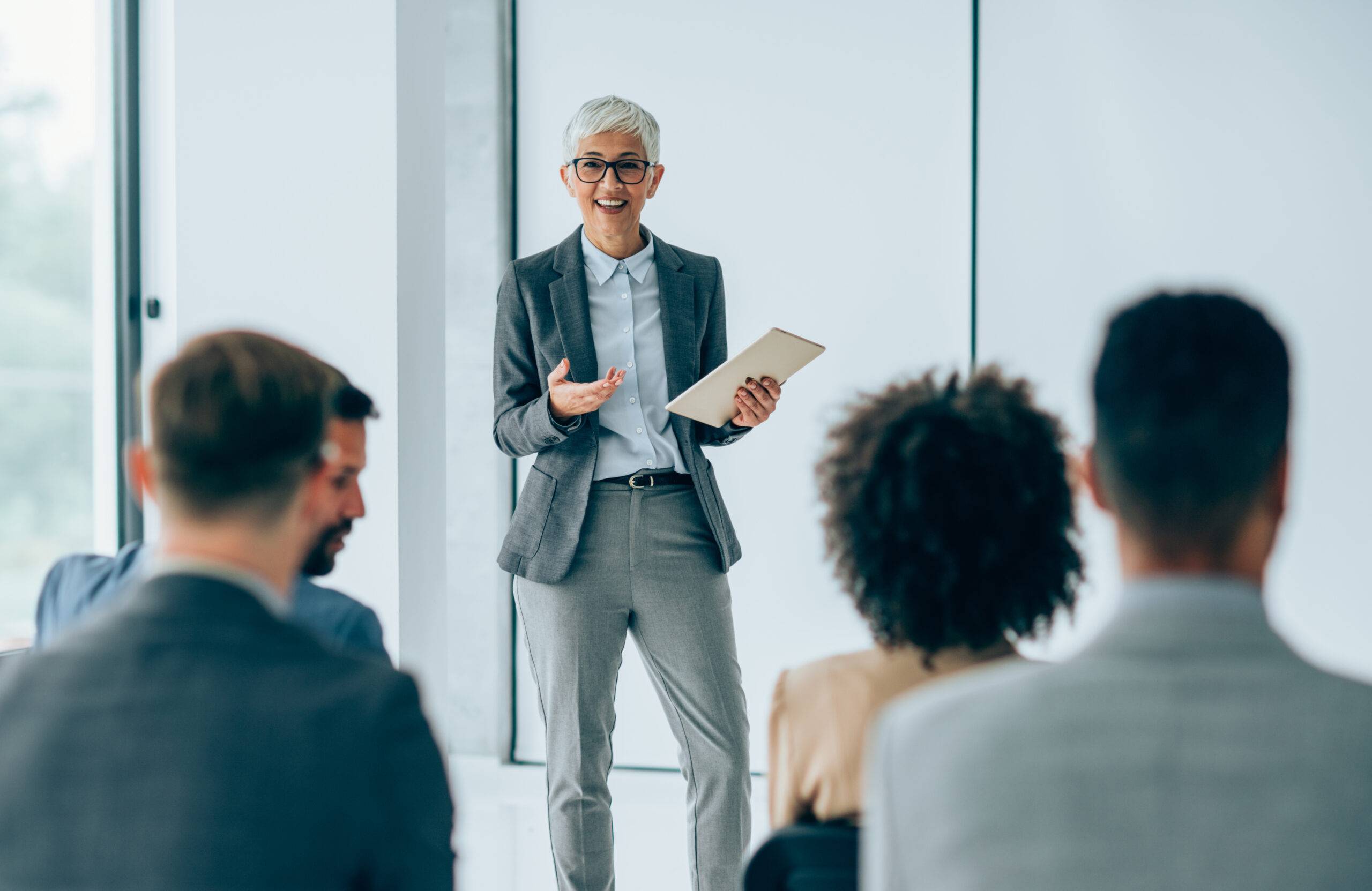 A person in a grey pantsuit wearing spectacles is instructing a group of candidates about the talent acquisition process.
