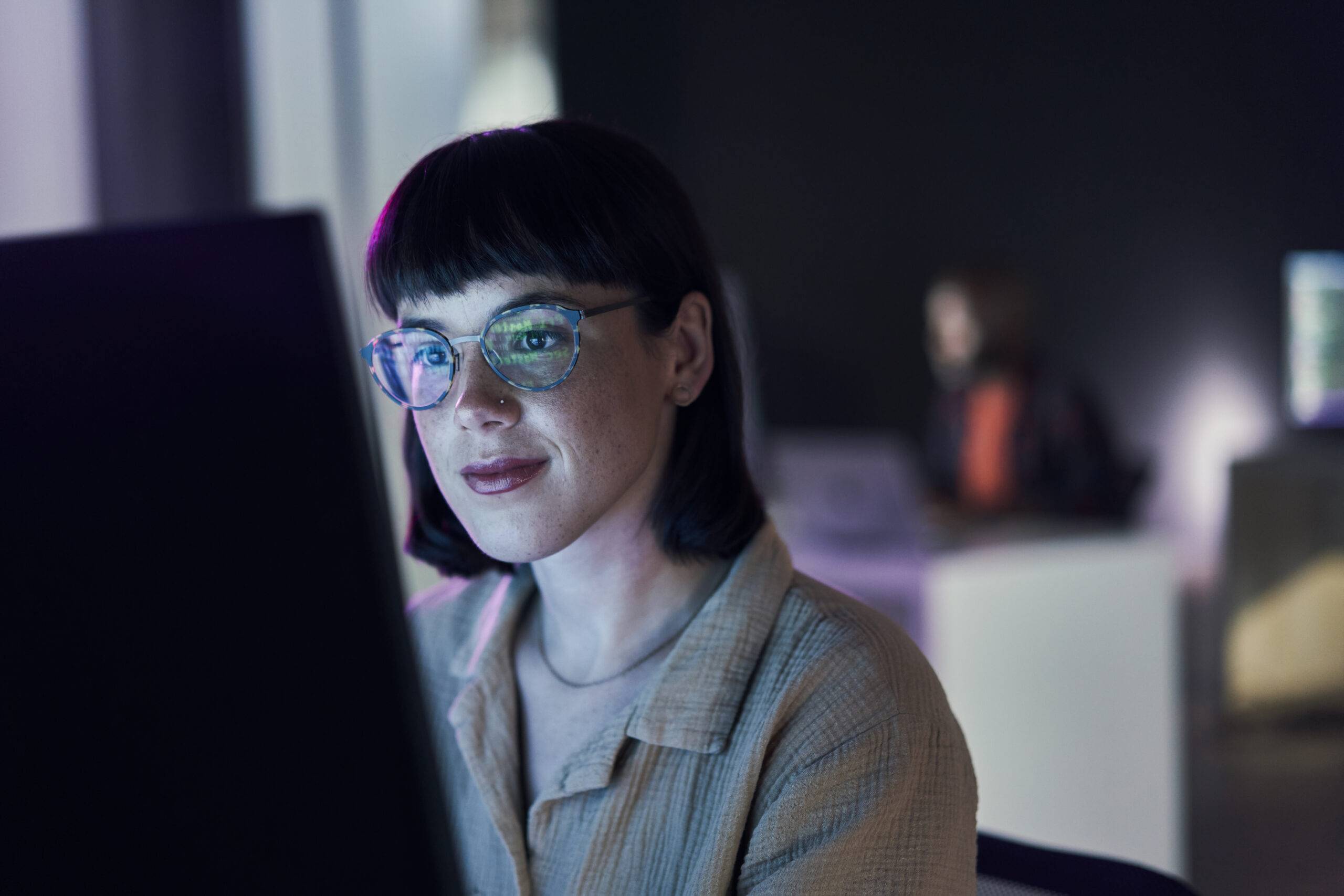 A woman with glasses is looking at the laptop screen at her workplace, analyzing employee sentiment data.