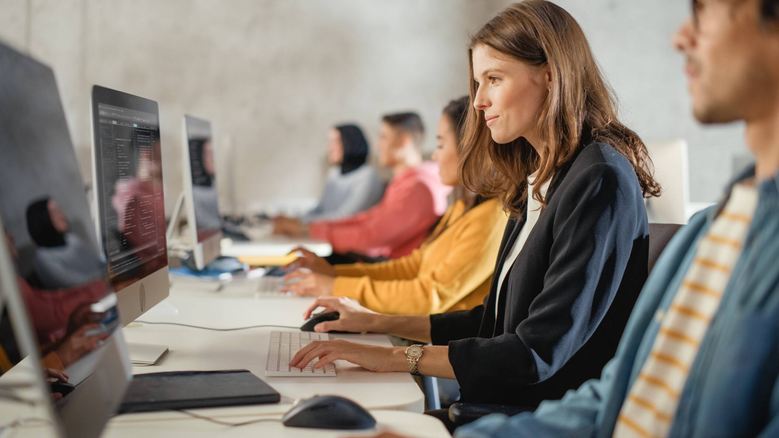 A female employee in a blue blazer along with other employees is taking an employee training on her computer.