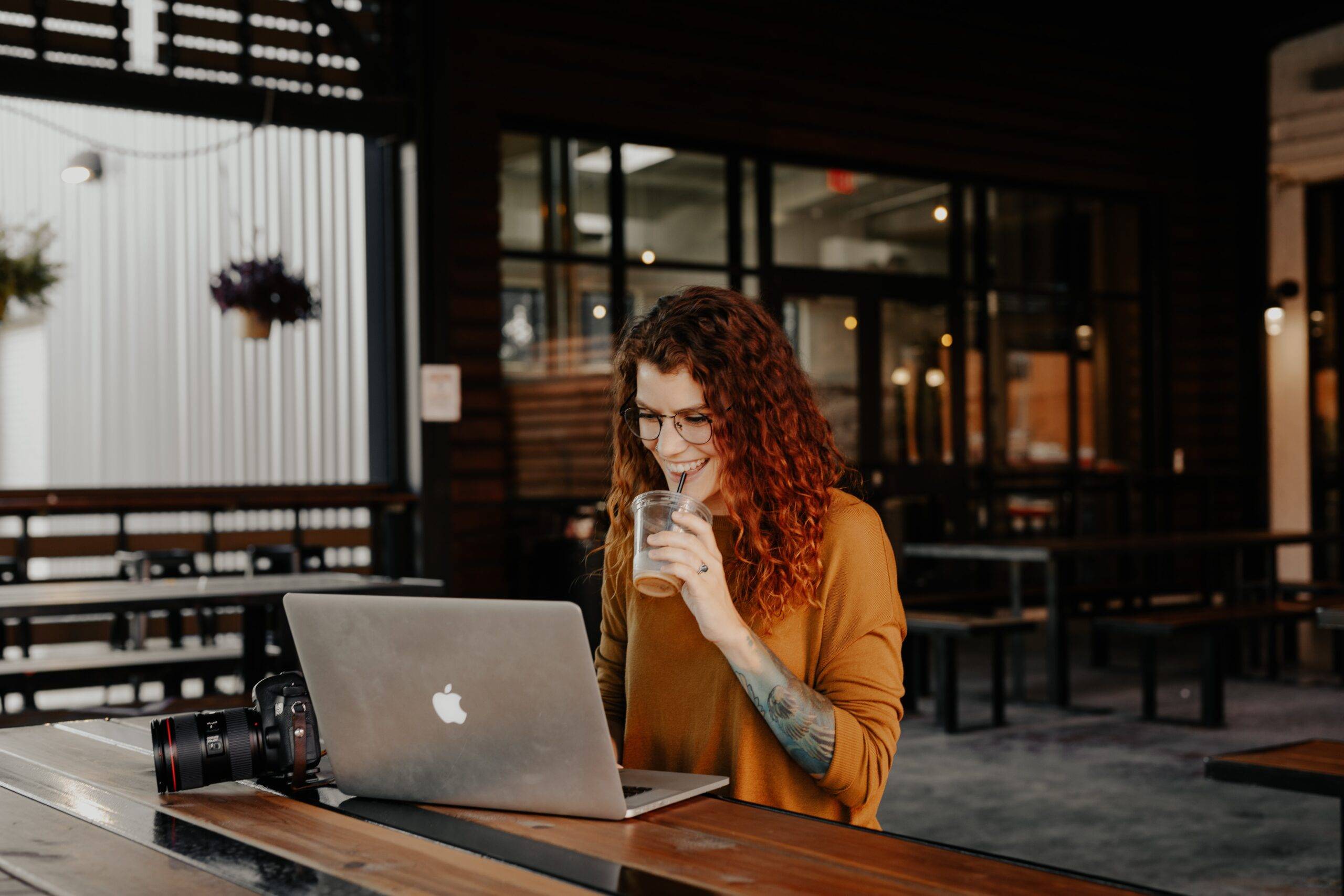Employee generated content: Woman smiling and drinking her beverage while working on the laptop in a cafe.
