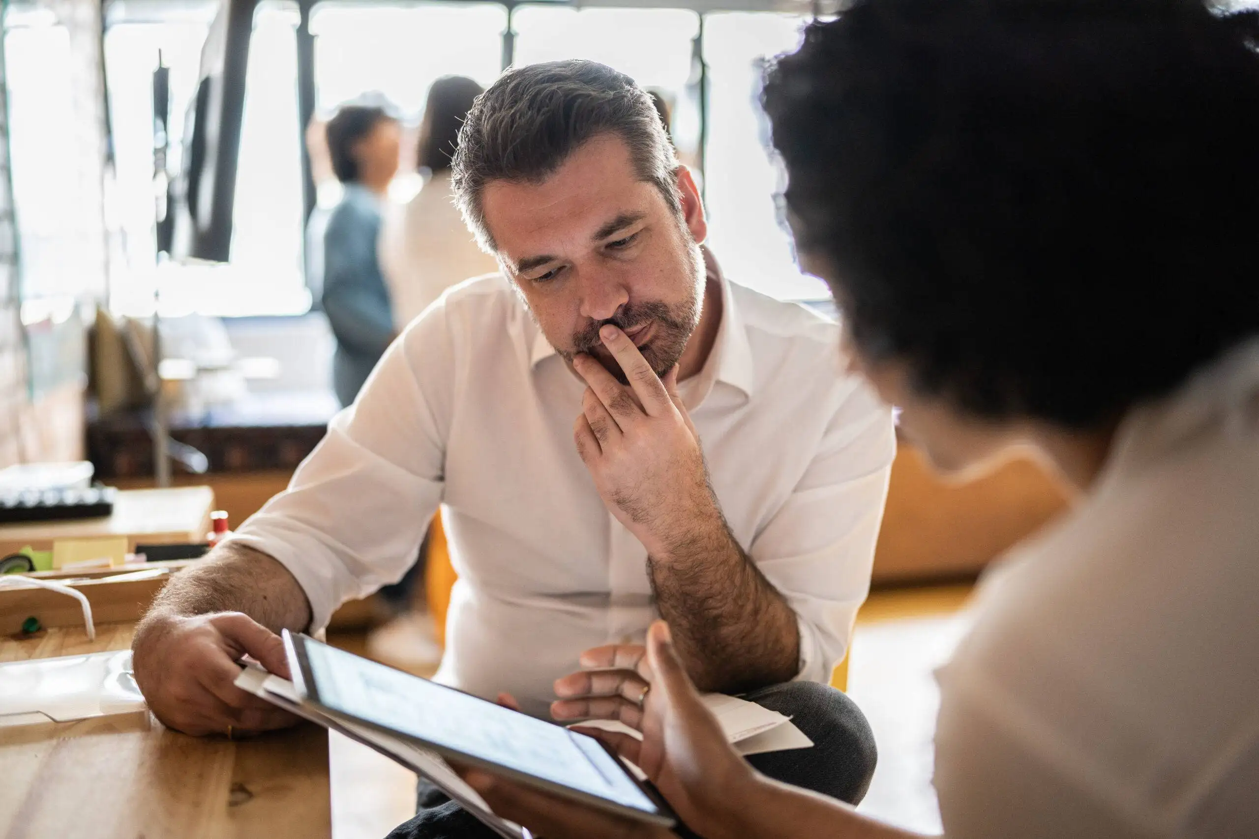 Performance management: a woman is showing her iPad to her colleague, who is thoughtfully considering the information displayed.