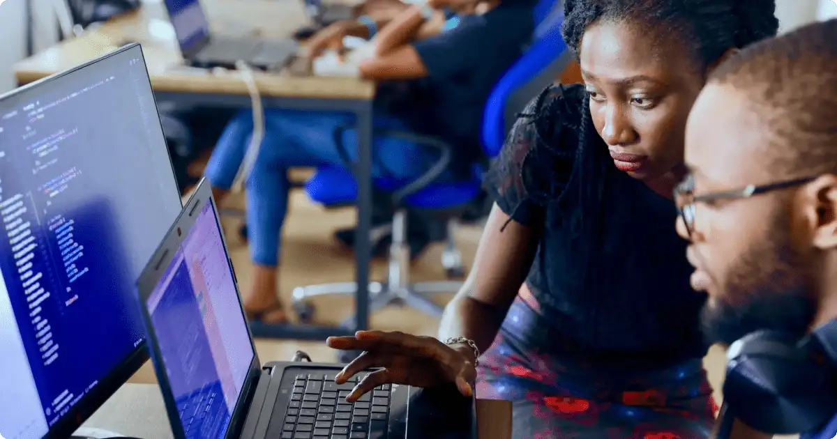 Learning management system (LMS): Two employees are working together on a laptop, engaging with an online training module in a collaborative workspace.