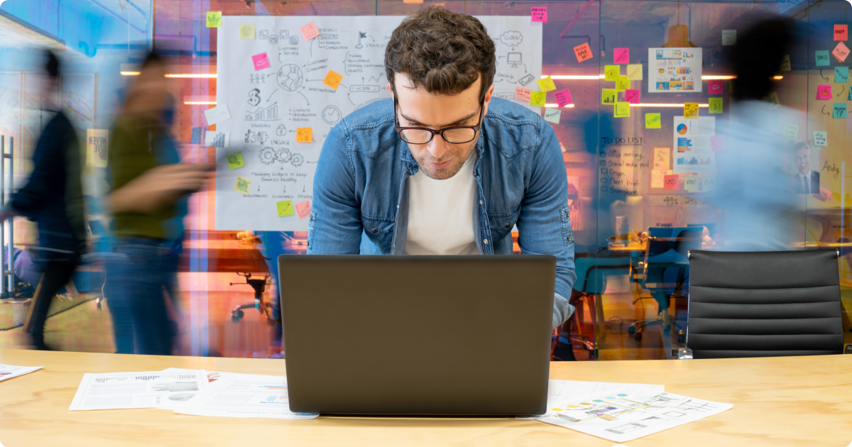 Shadow AI: A man in a blue shirt working on his laptop with a colourful blur background.